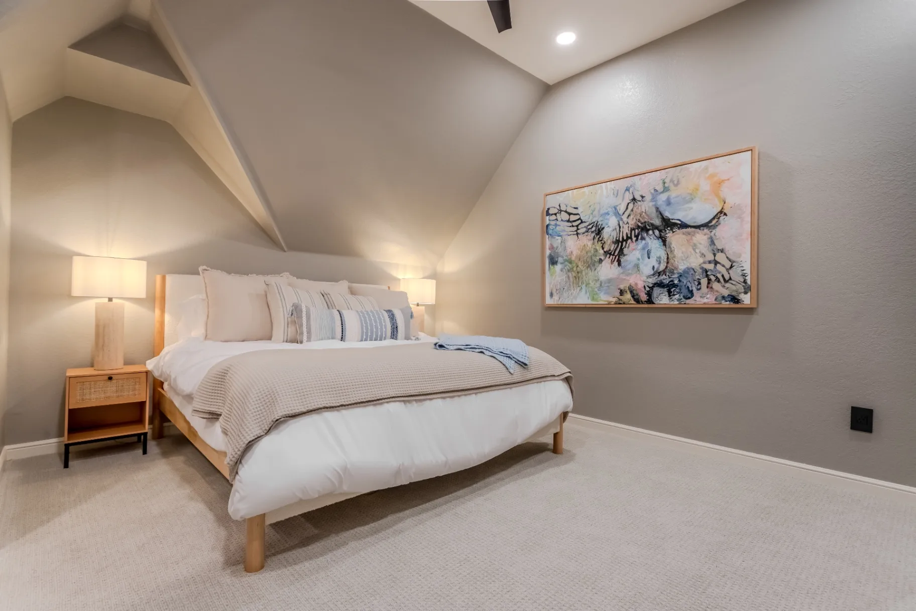 Finished guest bedroom with vaulted ceiling, plush carpet, and warm oak nightstands after the Broadmoor St remodel