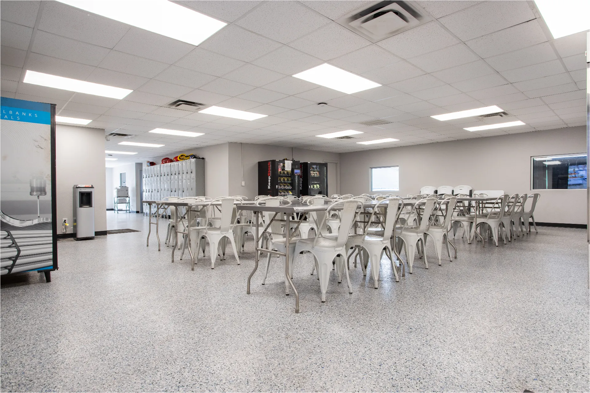 Employee breakroom dining area with folding stainless tables, metal chairs, lockers, and vending in the finished Fort Worth buildout