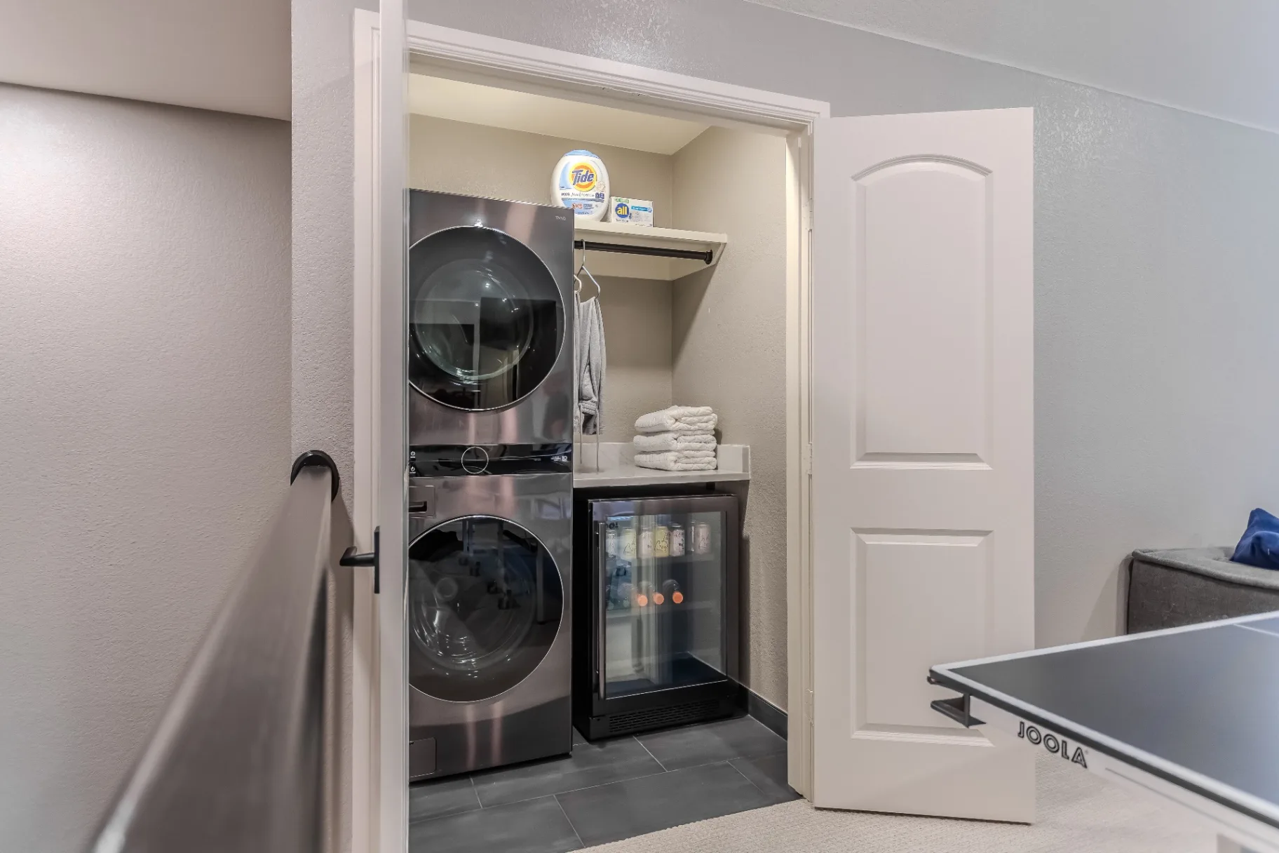 New stacked washer and dryer closet with shelving and beverage refrigerator off the game room