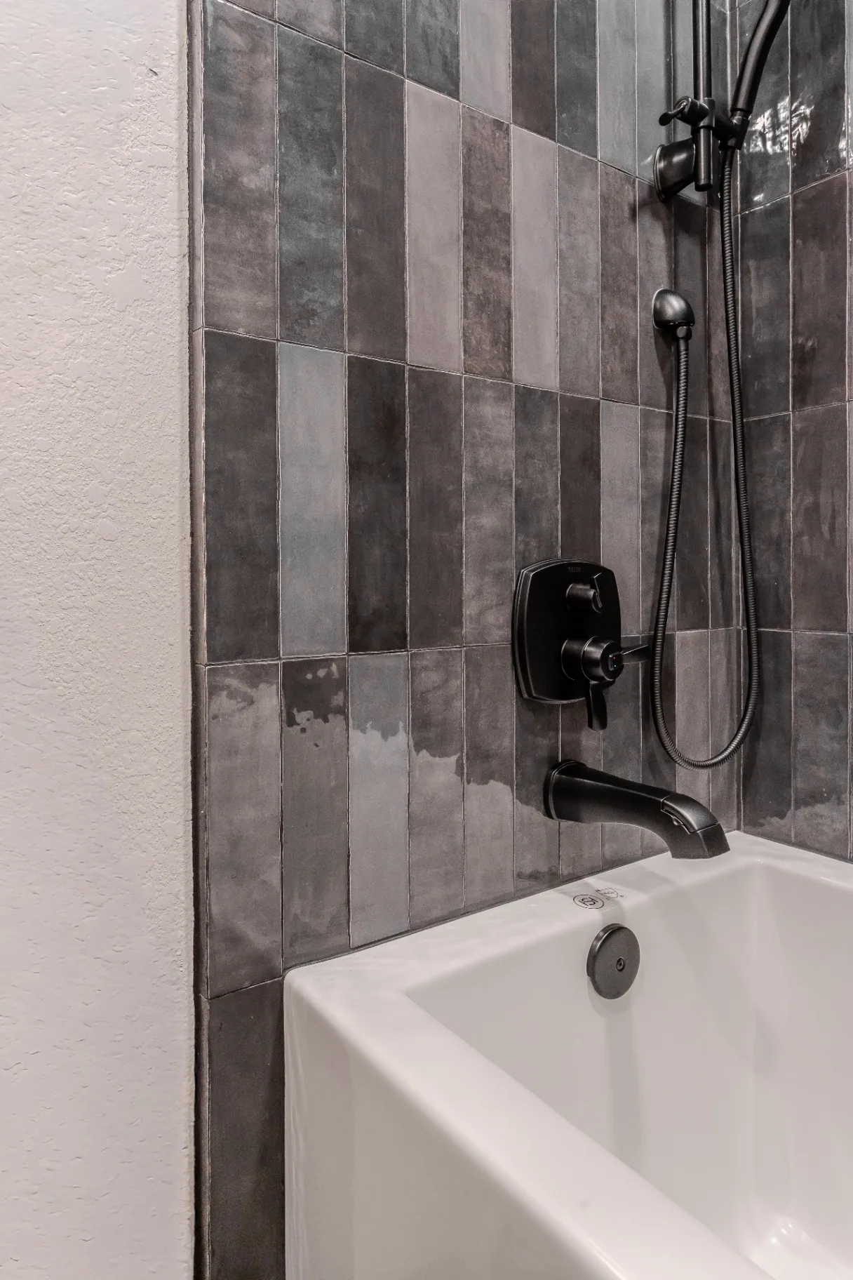 Detail of the charcoal zellige tile tub surround with matte black Delta tub and hand-shower trim