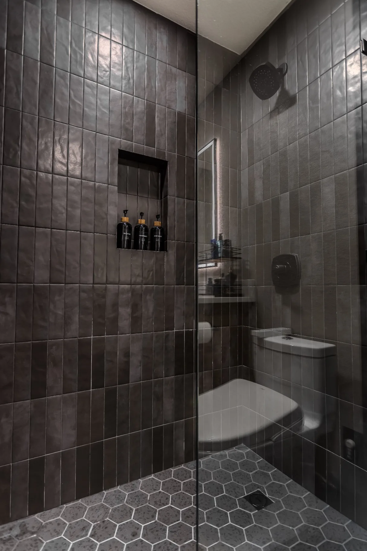 Walk-in shower interior with recessed tile niche, rainhead, and gray hexagon mosaic floor